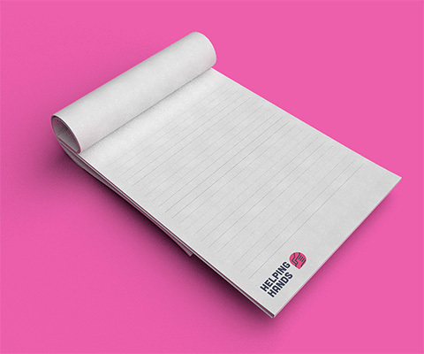 A lined notepad with "Helping hands" branding sitting on a pink background.