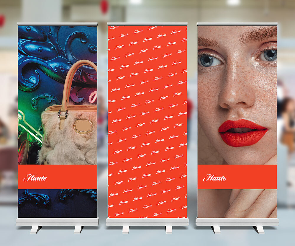 Three pull-up banners for Haute fashion. The banner on the left is an image of a purse on a bright background. The middle one is a red banner with the Haute logo repeated. The right one is a woman with red lipstick and blue eyes.