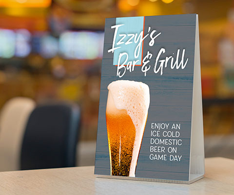 A gray Izzy's Bar & Grill folded triangular table topper with an image of large beer glass overflowing. The text reads "Enjoy an ice cold domestic beer on game day."