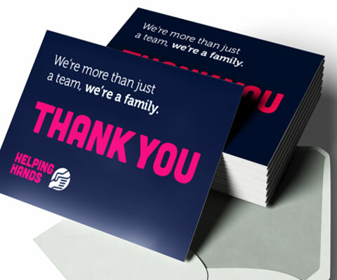 A stack of blue Thank You cards with white and pink text: "we're more than just a team, we're a family" and the helping hands logo.